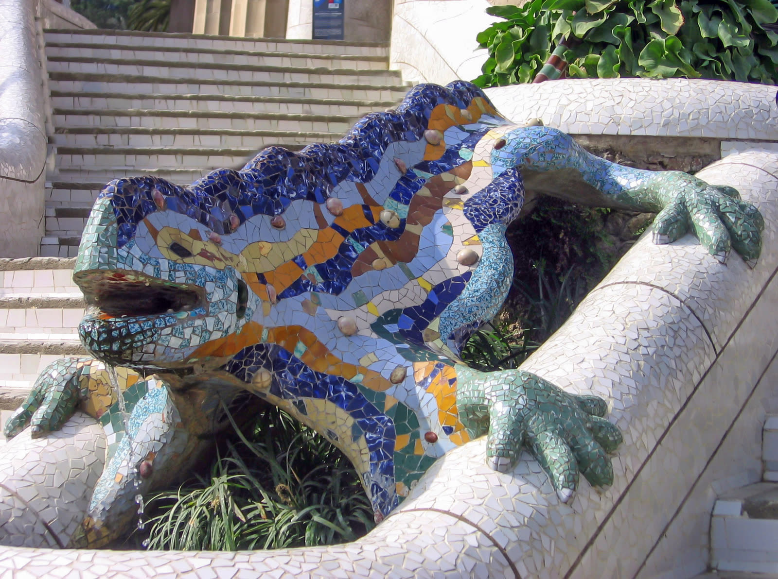 The famous mosaic salamander — ‘el Drac’ — at Park Güell, tiled in blue, green, yellow, and orange ceramic shards, sprawling across a white-tile fountain pedestal