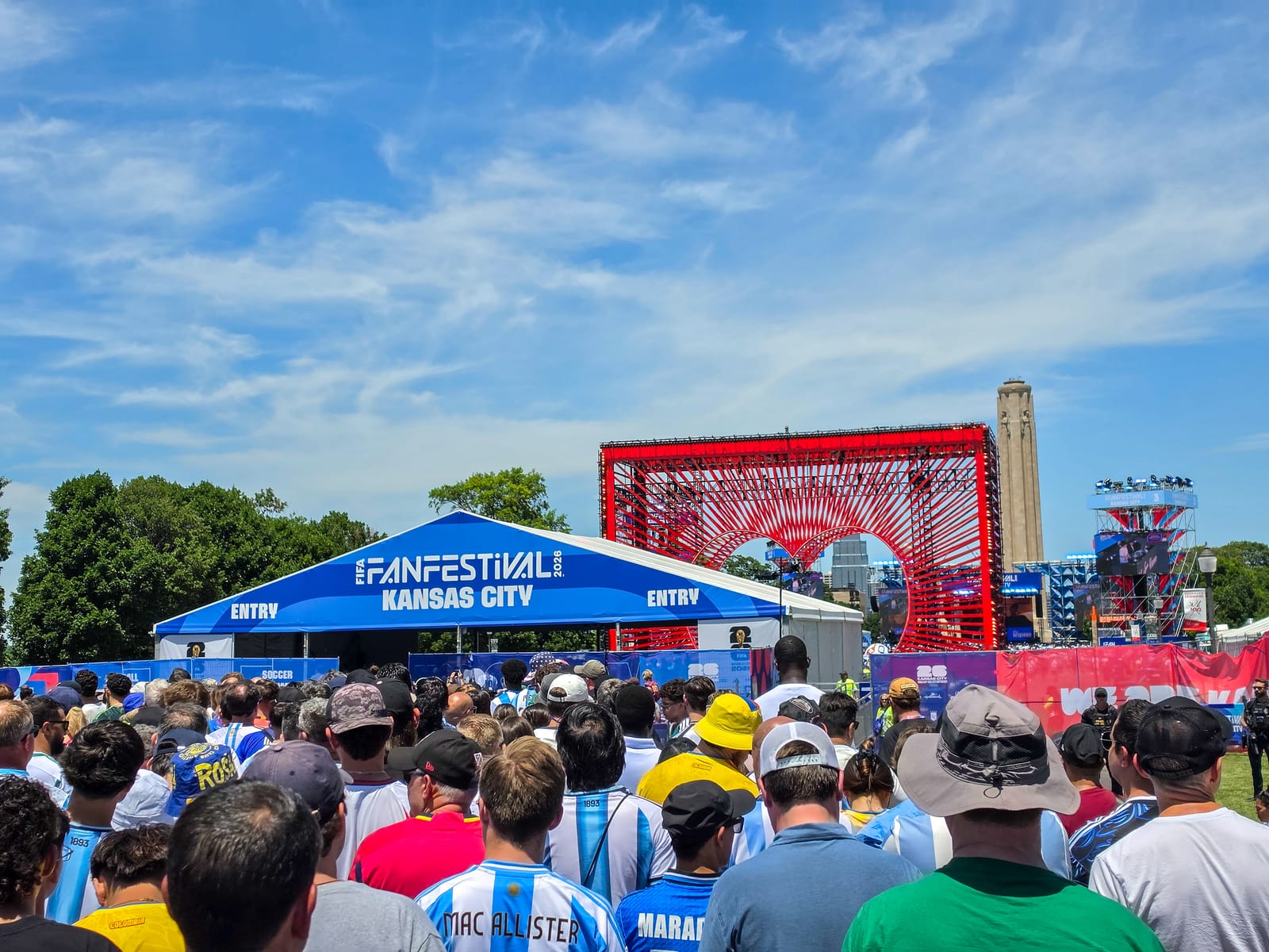 Crowd waiting to enter the World Cup Fan Festival in Kansas City, with a blue entry tent and a large red arch installation ahead