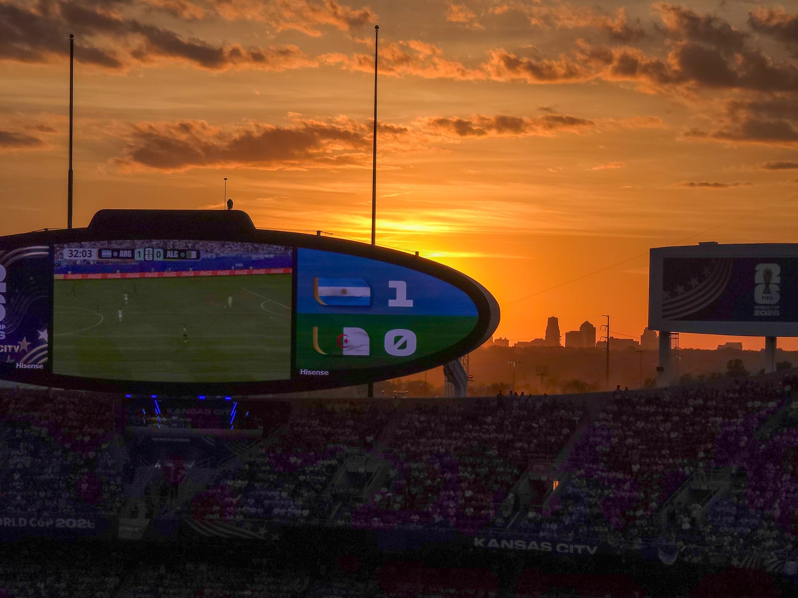 Sunset over the Kansas City skyline behind the stadium scoreboard during the World Cup, the score reading Argentina one, Algeria zero