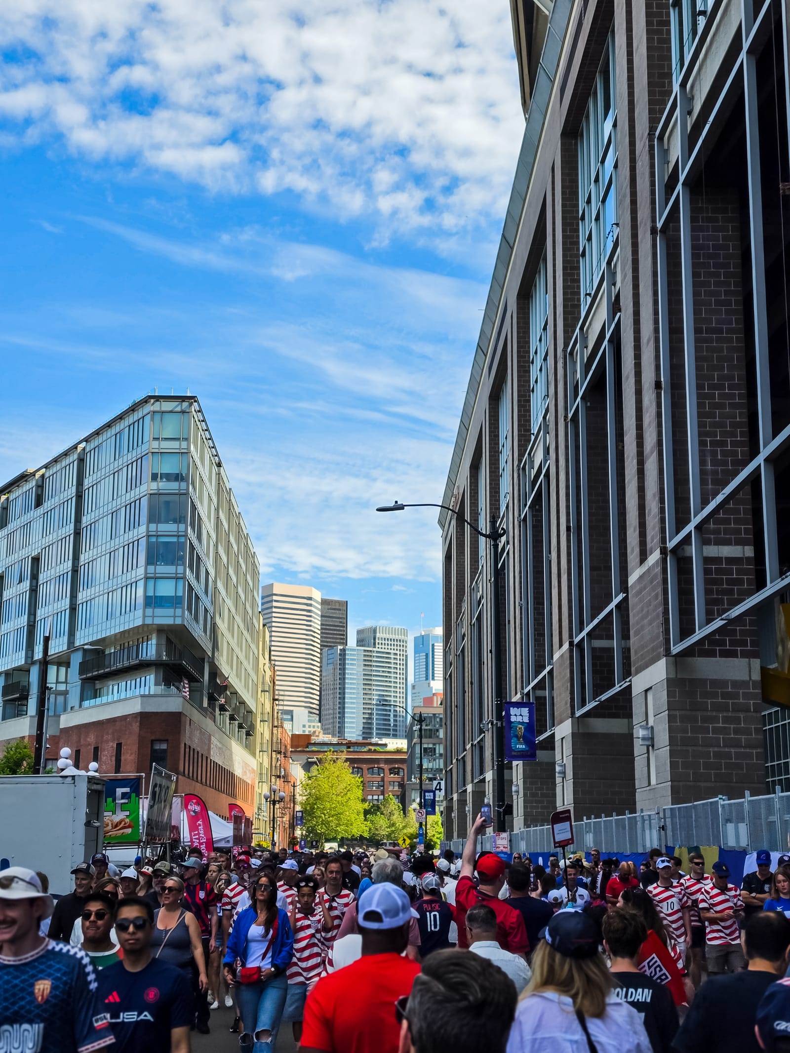 A crowd of United States supporters walking toward the stadium in Seattle on matchday, with the downtown skyline behind them under a clear blue sky